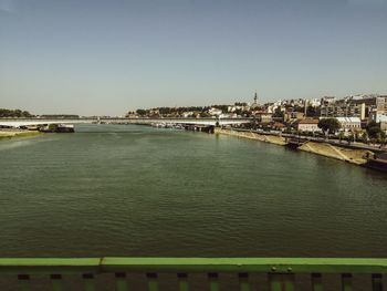 Bridge over river by buildings against clear sky