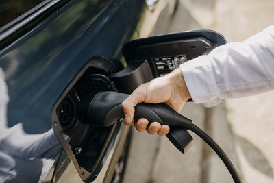 Man holding electric plug of hybrid car at charging point