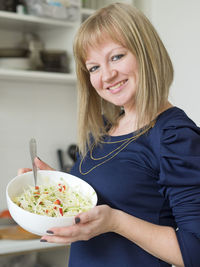 Smiling young woman with salad at home