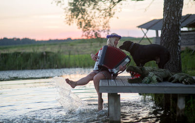 Full length of woman holding accordion with dog and crocodile toy on table by lake