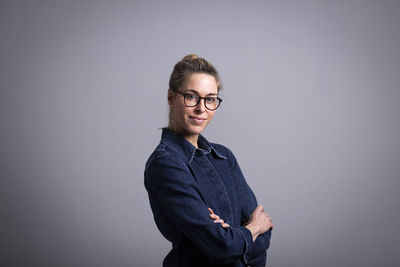 Businesswoman wearing eyeglasses standing arms crossed against gray background