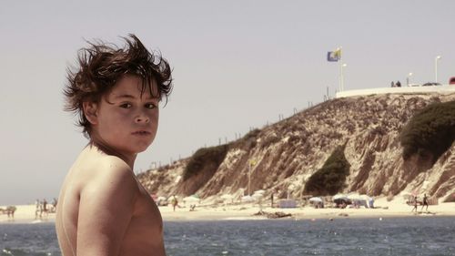 Portrait of shirtless boy at beach against sky