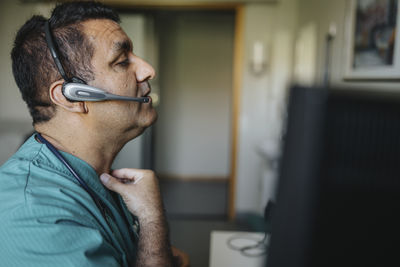 Side view of doctor touching throat giving advice through video call in hospital