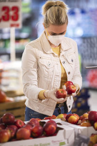 Teenage girl wearing protectice mask and gloves choosing apples at supermarket