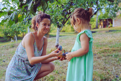 Side view of mother and daughter holding easter eggs on grass