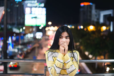 Portrait of woman standing against illuminated city at night