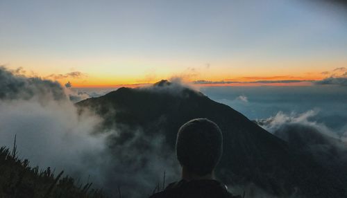 Rear view of man sitting against mountains during sunset