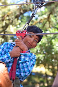 Low angle portrait of teenage boy on zip line against trees