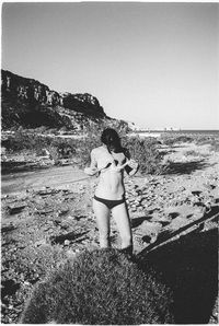 Rear view of woman standing on beach against clear sky