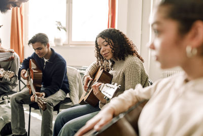 Smiling teenage girl practicing guitar with friends in music class at high school