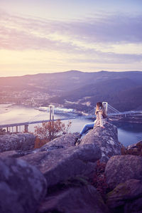 Woman sitting on rocks against sky during sunset