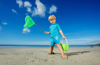 Rear view of man holding umbrella at beach against blue sky