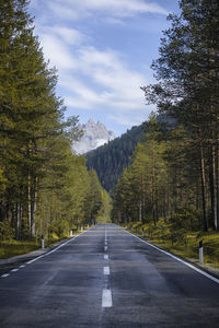 Empty road along trees and plants against sky