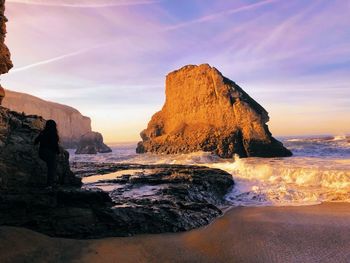 Rock formation on beach against sky during sunset