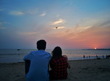 Rear view of people at beach during sunset