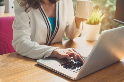 Midsection of woman with coffee using laptop on table