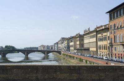 Arch bridge over river by buildings against sky