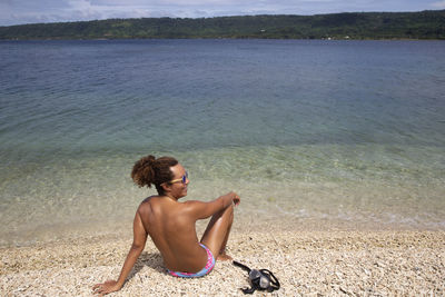 Full length of shirtless man sitting on beach