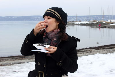 Woman eating seafood against lake during winter