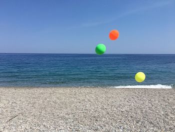 Multi colored balloons on beach against blue sky