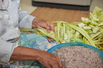 Hands of senior woman wrapping the sticky rice with palm leaf or ketupat palas