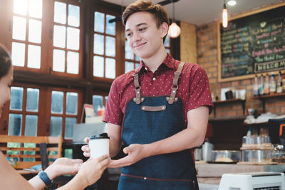 Barista serving coffee in cup to customer at cafe