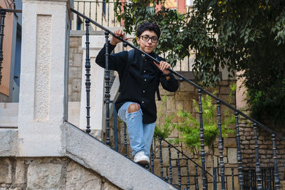 Young transgender person smiling while posing standing on stairs outdoors.