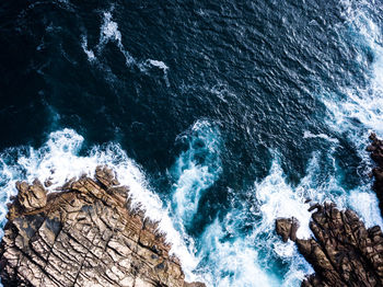 High angle view of waves splashing on rock formations at beach