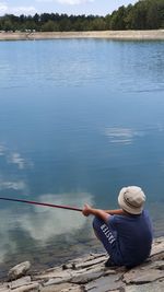 Rear view of man sitting by lake