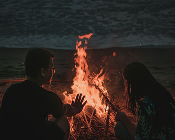 Couple by bonfire at beach during sunset