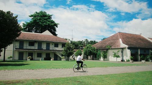 Man cycling on house against sky