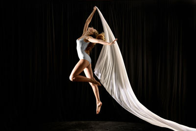 Side view of woman dancing against black background