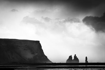 Scenic view of rock formations by sea against cloudy sky