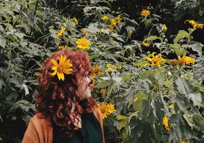 Redhead woman standing by yellow flowers blooming outdoors