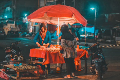 Rear view of people standing on illuminated street at night