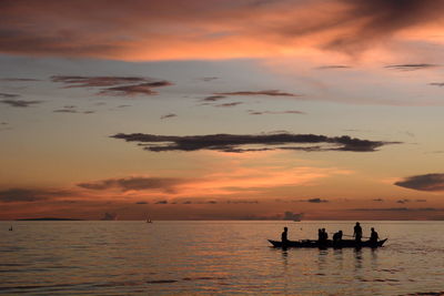 Silhouette people in sea against sky during sunset