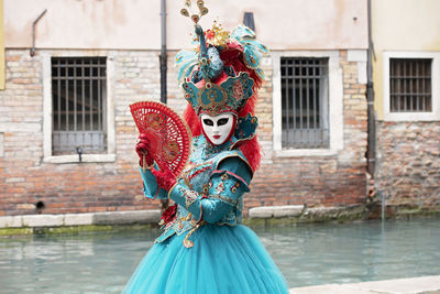 Woman in carnival costume standing by canal in city