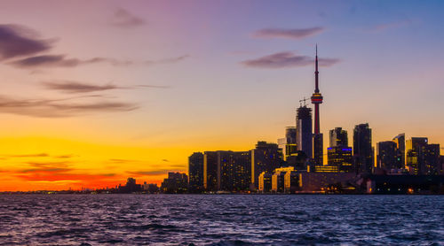 Sea by cityscape against sky during sunset