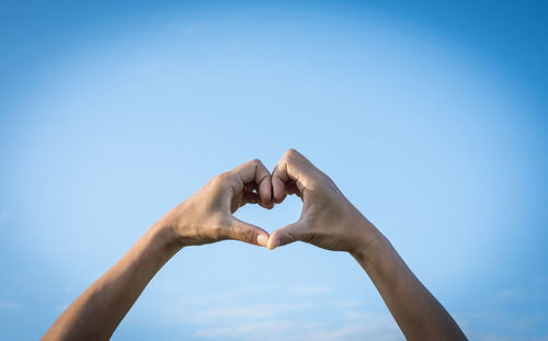 Low angle view of hand holding heart shape against clear blue sky