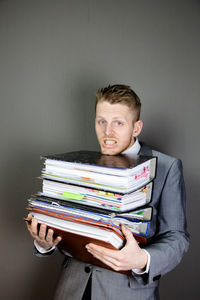 Tired businessman holding stacked files against gray background