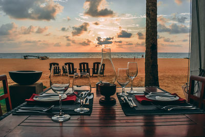 Chairs and tables at beach against sky during sunset