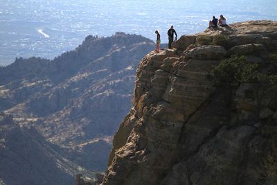 People on cliff by mountains against sky