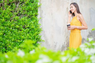 Young woman using mobile phone while standing on plants