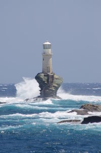 Lighthouse on beach by sea against sky