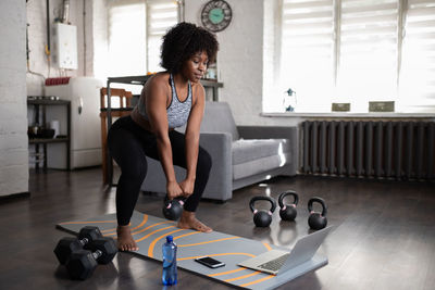 Ethnic sportswoman lifting kettlebell during online training