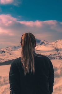 Rear view of woman on snow covered mountain standing against sky during sunset