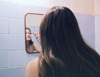 Rear view of woman applying make up at bathroom