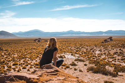 Rear view of woman sitting on land against sky