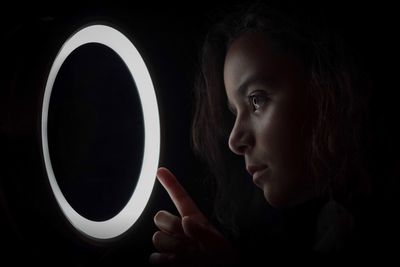 Close-up of girl looking at illuminated circle against black background