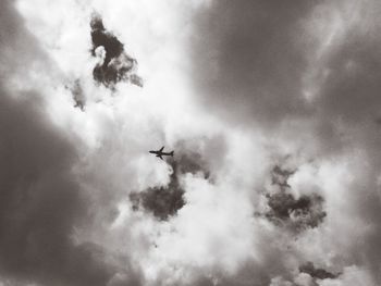 Low angle view of airplane flying against cloudy sky